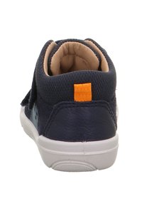 Marineblauwe enkelschoenen met een gestructureerde stoffen bovenkant en oranje accent nabij de hiel, voorzien van een witte rubberen zool en klittenbandsluiting.