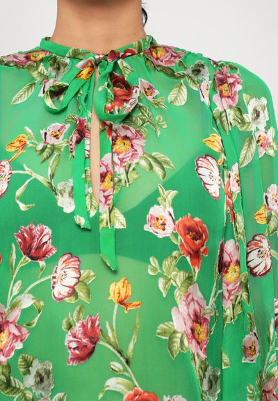 Green floral blouse featuring a high neckline with tie detail, sheer fabric, and multicolored flower patterns on the front.