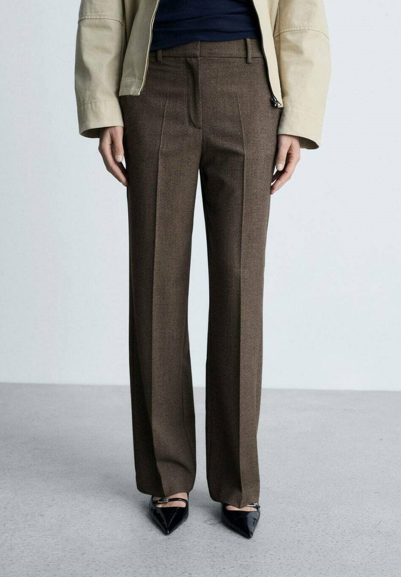 Pantalons marron ajustés en tissu texturé avec une coupe droite. Comprend des plis avant et une taille haute, associés à des chaussures noires pointues.