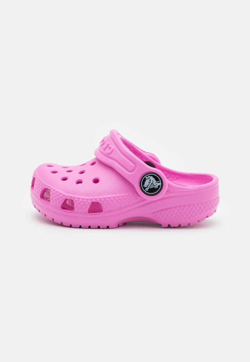 Pink rubber clog with ventilation holes, adjustable strap, and textured sole. Features a circular logo on the side near the strap.