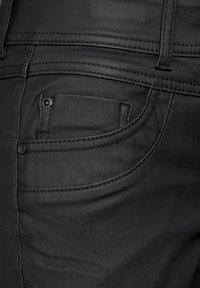 Svarta denimjeans med en närbild av en sidoficka som framhäver den släta texturen, detaljerad sömnad och metallknappar.