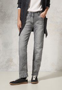 Jeans in denim grigio con una texture vissuta, caratterizzati da un taglio a gamba dritta, chiusura a due bottoni e dettagli di cucitura discreti. Abbinati a sneakers nere.