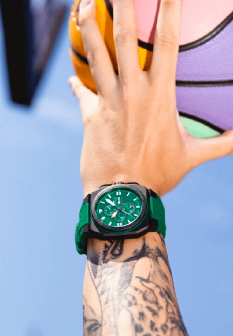 Zelené športové hodinky s okrúhlym ciferníkom, čiernym a zeleným silikónovým remienkom, textúrované detaily, zobrazené na ruke, ktorá drží basketbalovú loptu.