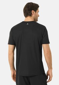 Černé sportovní tričko s krátkými rukávy. Texturovaná tkanina, jednoduchý design a malé logo na krku. Zdůrazňuje komfort a pohyblivost.