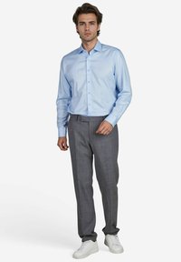 Lichtblauwe overhemd met lange mouwen, grijs patroonbroek en witte sneakers. Het overhemd heeft een button-down kraag en een gladde textuur.