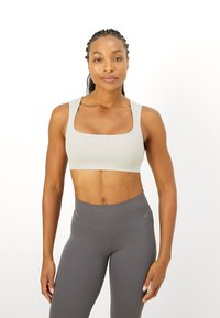Sujetador deportivo gris claro con escote cuadrado y tirantes anchos, hecho de material elástico. Combinado con leggings de cintura alta gris oscuro.