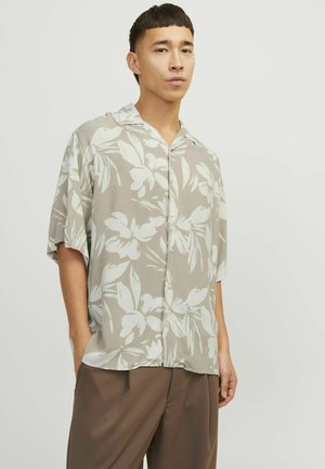 Short-sleeve button-up shirt in light beige with large white floral patterns. Made of smooth fabric with a relaxed fit and camp collar.