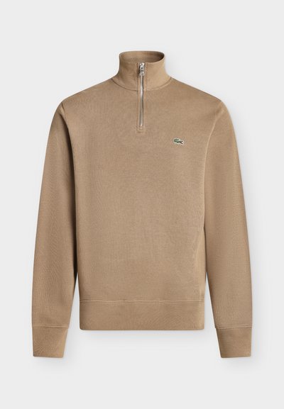 Pull beige à manches longues avec col zippé jusqu'au quart et petit logo crocodile vert sur la poitrine gauche.