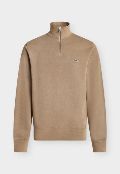 Pull beige à manches longues avec col zippé jusqu'au quart et petit logo crocodile vert sur la poitrine gauche.
