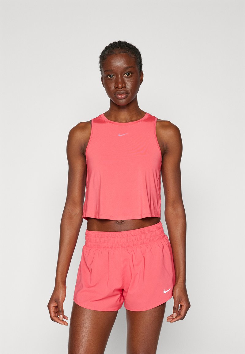 Top corto deportivo rosa y pantalones cortos hechos de tela ligera, con un escote redondo y acentos del logo de Nike en ambas piezas.