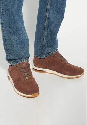 Brown suede sneakers with a white midsole and rubber outsole, featuring lace-up design and textured fabric accents.