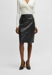 Black leather pencil skirt featuring a streamlined design with front seams, knee-length cut, and subtle texture. Worn with a light-colored top.