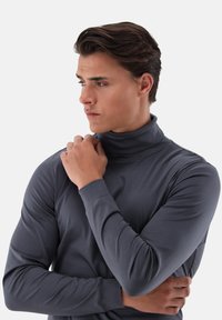 Grauer Rollkragenpullover aus glattem Stoff; figurbetontes Design mit langen Ärmeln; keine sichtbaren Muster oder Verzierungen. Schlichtes, modernes Aussehen.
