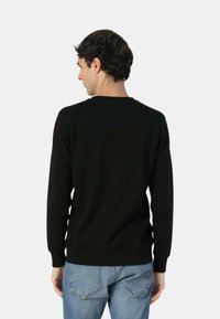 Maglione nero con maniche lunghe, scollo e orlo a costine. Indossato con jeans denim blu. Tessuto liscio, taglio aderente, design minimalista.