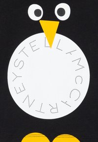 Černé tričko s grafikou tučňáka, velkým bílým kruhem a tečkovaným písmem, oranžovým zobákem a žlutými nohama na spodní části.