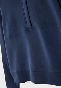 Gros plan d'un sweat-shirt bleu marine montrant la texture du tissu et les détails des coutures près de la poche et de l'ourlet.