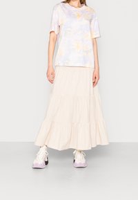 Licht paarse tie-dye t-shirt met korte mouwen, gecombineerd met een lange beige gelaagde rok, gedragen met witte en lavendel sneakers.