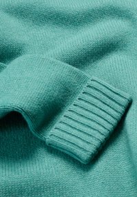 Tirkizno pletena dukserica s rebrastim rubovima. Glatka tekstura, ravnomjerno šivanje. Tkanina je lagana i izdržljiva, s mekim završetkom.