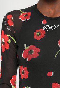 Svart langermet topp med røde blomstertrykk, mesh-ermer og broderte logo-detaljer. Glatt tekstur med en tettsittende design.