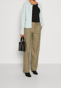 Cardigan de punto azul claro, top negro ajustado, pantalones de cintura alta verde oliva, bolso negro con asa trenzada y botines negros con tacón.