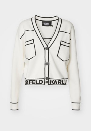 Bela kardigan s črnimi obrobe, sprednjimi gumbi in dvema žepoma na prsih. Ima skrajšan kroj in označen rob z besedilom "KARL".