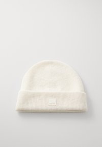 Balts adījuma beanie ar ribotu tekstūru un salocītu apkakli, ar nelielu kvadrātveida etiķeti priekšpusē. Mīksts, viegls materiāls.