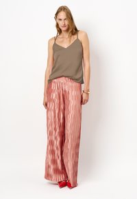 Satin bruine cami-top met dunne bandjes, gecombineerd met wijde, geplooide rozenroze broek en rode blokkengels. Glad textuur en vloeiend ontwerp.