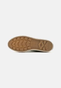 Suola in gomma per sneaker con una presa dettagliata e strutturata; presenta un colore beige chiaro e un logo rotondo sul superficie della suola.