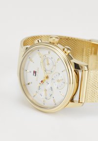 Goldfarbener Chronograph mit einem strukturierten Mesh-Armband, weißem Zifferblatt, blauen Akzenten, drei kleinen Zifferblättern und auffälligen Stundenmarkierungen.