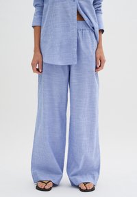 Svetle modrá pruhovaná košile a široké kalhoty, vyrobené z měkké tkaniny. Kalhoty mají elastický pas a volný střih.