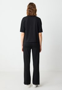 Czarny, luźny top z krótkim rękawem w połączeniu z czarnymi spodniami o prostym kroju, wykonanymi z miękkiego materiału. Posiada prosty design i czyste linie.