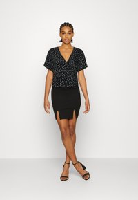 Blusa de manga curta com padrão floral preto e decote em V, combinada com uma saia justa preta com fendas laterais, complementada por sandálias de salto pretas.