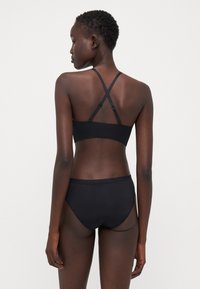 Black bralette and matching high-waisted briefs with scalloped trim; made of smooth fabric; cross-back strap design on bralette.