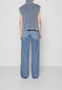 Ärmelloses, hochgeschlossenes, gestreiftes Oberteil in Marineblau und Weiß. Kombiniert mit weit geschnittenen, hellblauen Jeans aus Denim im klassischen Fünf-Taschen-Design.