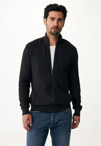Giacca nera con zip, dotata di un motivo testurizzato, adatta alla vestibilità slim e con polsini a costine. Indossata sopra una camicia bianca e abbinata a jeans blu.