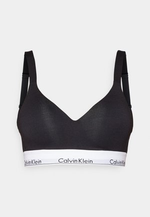 Zwarte bralette met een V-halsontwerp, textuur stof, verstelbare bandjes en een witte Calvin Klein logo band eronder.