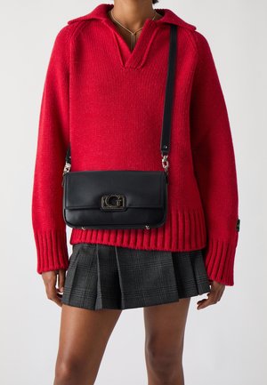 Rode gebreide trui met een kraag, gecombineerd met een zwarte textuur crossbody tas met een metalen sluiting, en een geplisseerde grijze geruite rok.