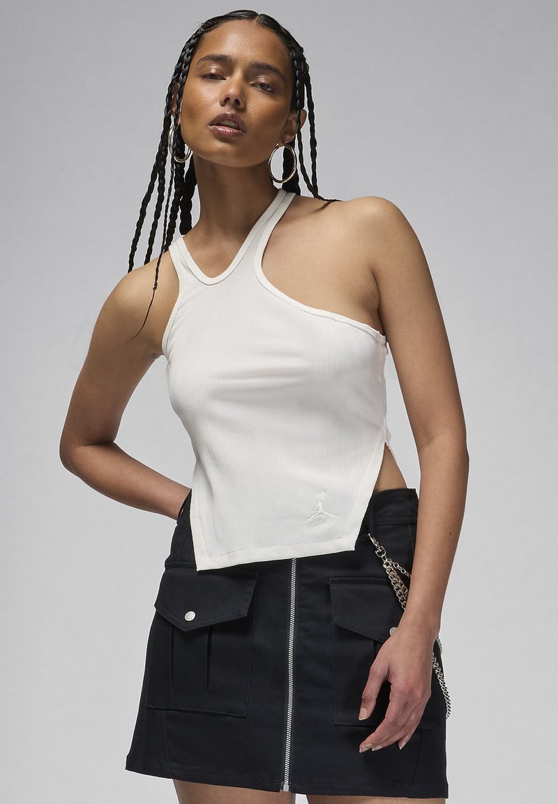 Top in cotone bianco a coste con un taglio asimmetrico, caratterizzato da un piccolo logo. Indossato con una gonna nera con zip frontale e tasche.