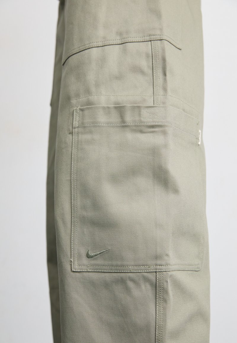 Pantaloni cargo in tessuto verde oliva chiaro con finitura testurizzata, dotati di tasche laterali e un piccolo logo Nike sulla tasca.