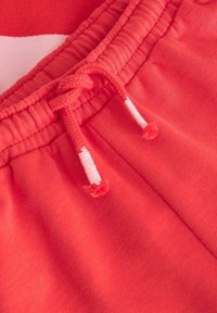 Pantalons de survêtement corail avec une taille élastique dotée d'un cordon de serrage blanc contrastant et de détails de couture visibles sur le tissu.