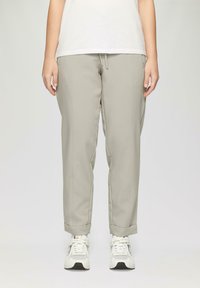 Lichtgrijze tappered broek met een trekkoord in de taille en opgerolde boorden, gemaakt van een gladde stof. Gecombineerd met witte sportschoenen.