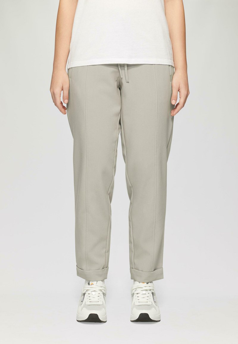Lichtgrijze tappered broek met een trekkoord in de taille en opgerolde boorden, gemaakt van een gladde stof. Gecombineerd met witte sportschoenen.