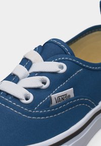 Μπλε αθλητικό παπούτσι Vans με λευκά κορδόνια, λευκή ραφή και λευκή λαστιχένια σόλα, με ετικέτα λογότυπου στο πλάι κοντά στα κορδόνια.