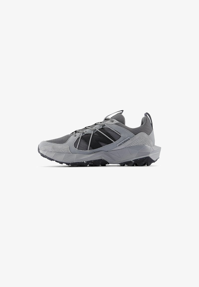 Chaussure de sport grise avec un upper en tissu maillé, des accents texturés, une semelle robuste et un système de laçage. Présente un logo noir sur le côté.