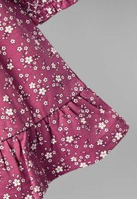 Stoff mit Blumenmuster in tiefem Mauve, der kleine weiße Blumen zeigt. Der Saum hat einen gerafften, gewellten Unterschied.