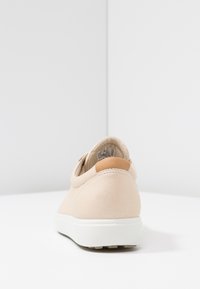 Beige sneaker with a smooth leather finish, rounded heel, and white rubber sole. Features a tan accent at the heel and minimal stitching.