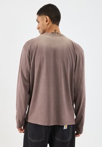 Pika-sleeve särk pehmest, heledast pruuni kangast, millel on gradient efekt. Omab ümmargust kaelust ja soonikstruktuuri. Silt on nähtav alumisel serval.