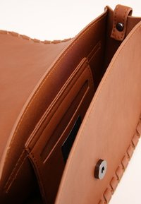 Borsa in pelle marrone con una texture morbida, dotata di chiusura a bottone e tasche interne per l'organizzazione. Il design enfatizza la praticità.