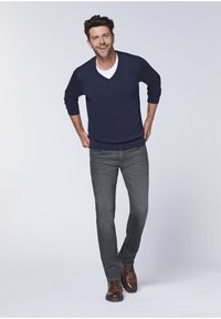 Dark blue v-neck sweater over a white t-shirt, paired with gray jeans and brown shoes. The outfit features a relaxed fit and simple design.