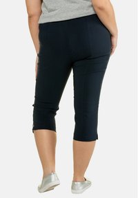 Navy capri broeken met een getailleerd ontwerp, voorzien van splitten aan de onderkant. Gemaakt van een soepele, elastische stof, gedragen met zilveren instapschoenen.
